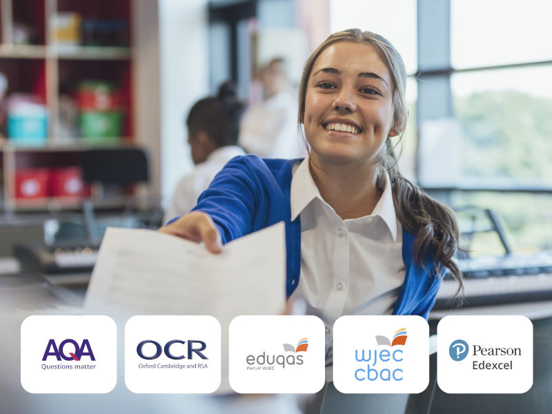 Smiling student in school uniform extending worksheet toward viewer in bright classroom, with exam board logos (AQA, OCR, Eduqas, WJEC CBAC, Pearson Edexcel) displayed below