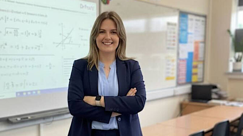 Female teacher standing confidently in front of a digital display showing Dr Frost Maths lesson content
